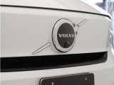 【ボルボの電気自動車を象徴するフロントフェイス】時代に合わせて変化するエンブレムデザイン。センターを斜めに大きく横切るラインと黒地に銀のアイアンマーク、これが最新ボルボのキャラクターアイコンです。