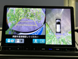後方の映像に加えて車両周辺の俯瞰表示も確認でき、駐車時の周囲確認をサポートします。画面上のガイド表示を目安にでき、狭い場所での切り返しにも便利です。